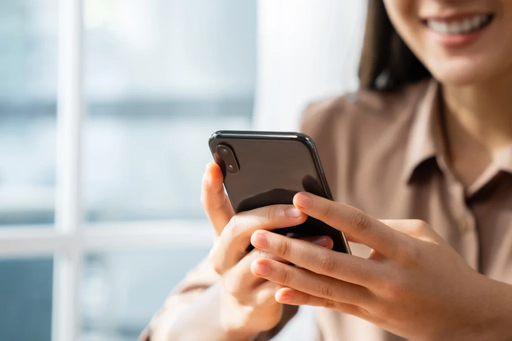 Smiling person holding and using a smartphone, representing mobile communication as part of a POTS Line Replacement strategy.